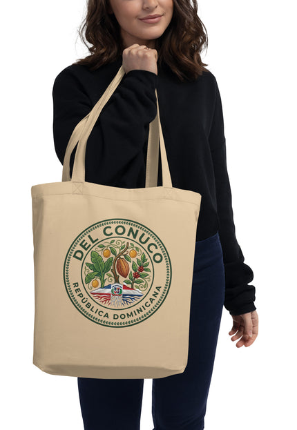 Natural organic cotton eco tote bag with Del Conuco Heritage Edition brand seal featuring cacao pod, banana leaves, coffee cherries, chinola vines, and Dominican flag at the base
